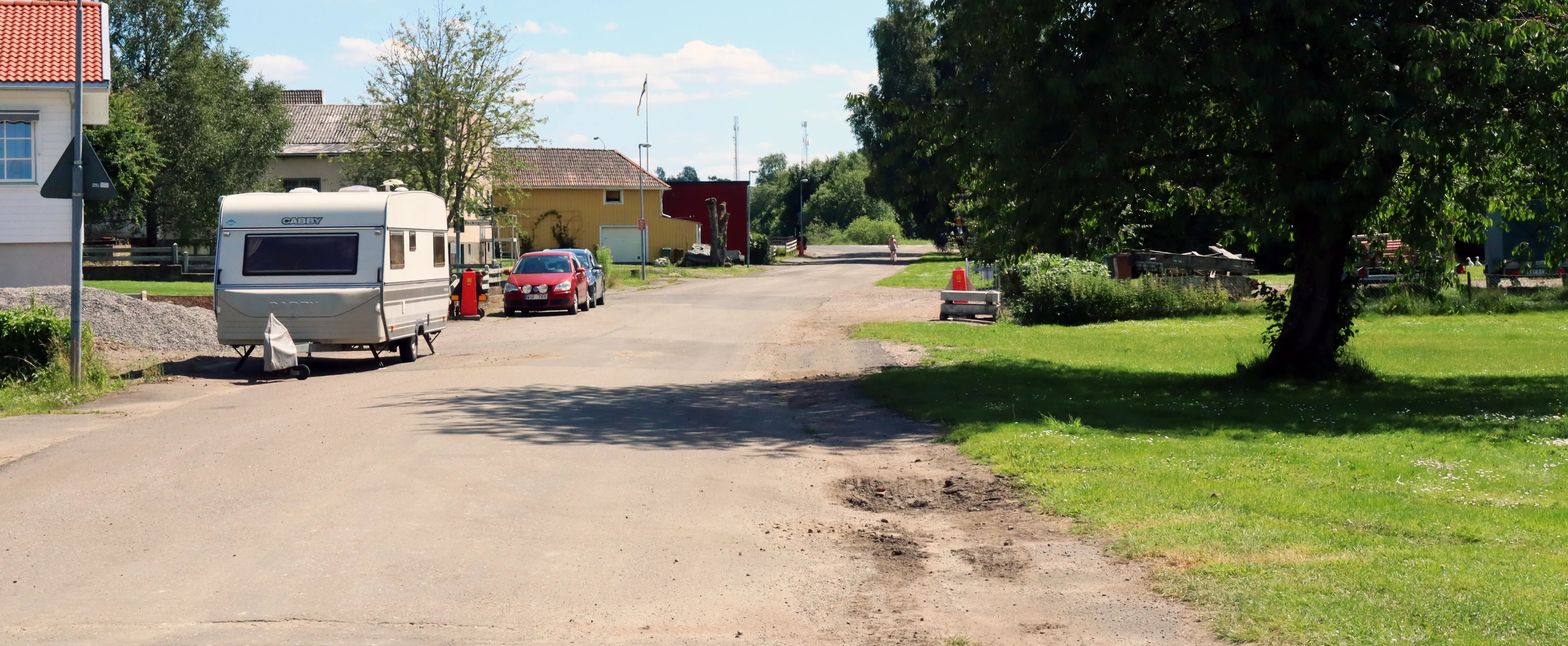 Gata med grönområde till höger. Parkerade bilar i bakgrunden.