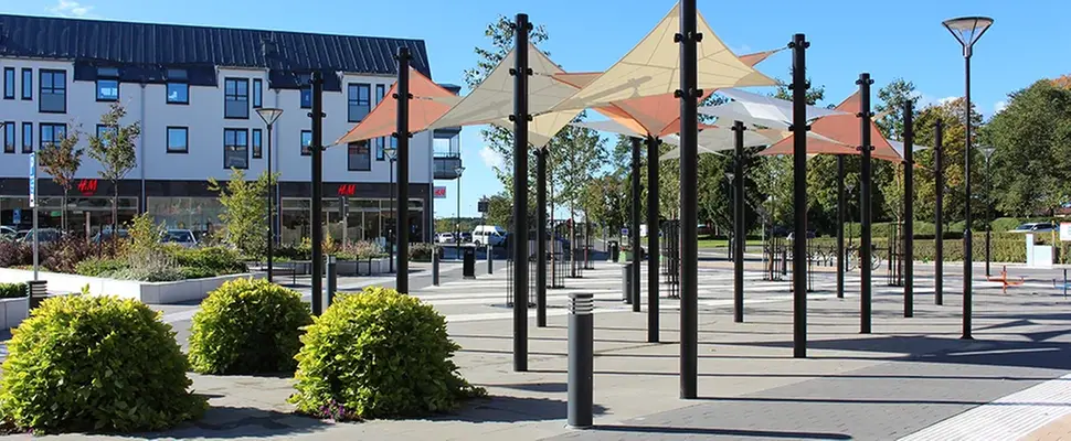 Köttorget med planteringar, hus i bakgrunden och flaggor i olika färger som ger skugga från solen.